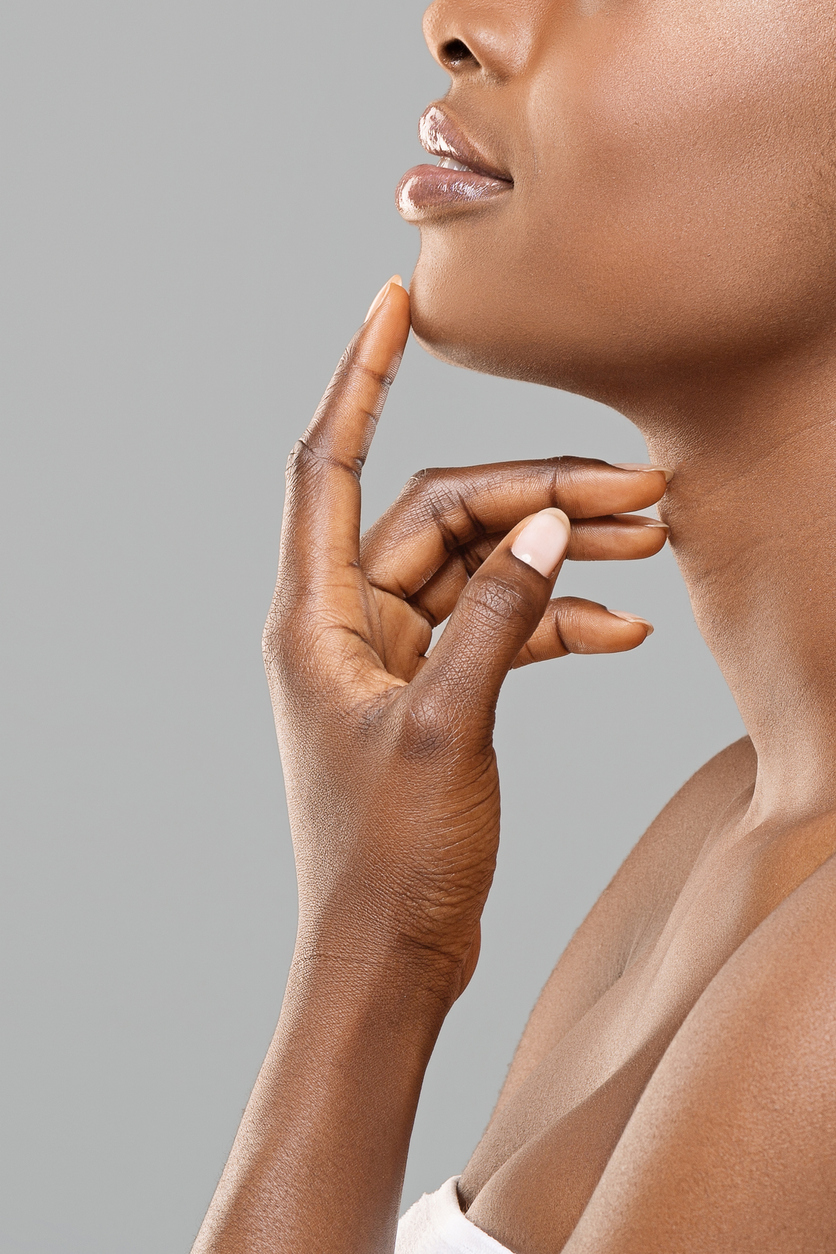 Chin augmentation. Unrecognizable afro woman touching chin implant in her face, happy with result of plastic surgery, gray background with free space