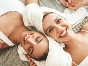 Two young beautiful smiling women in white bathrobes and towels on head. 300x225 1