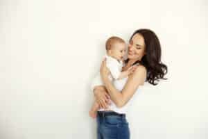 Slender woman holds a baby after breast lift and tummy tuck to improve her post-pregnancy body
