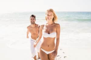 Woman in white bikini holds hands with her partner on the beach