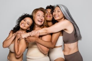 Diverse group of women in ages and ethnicities in their underwear hug.